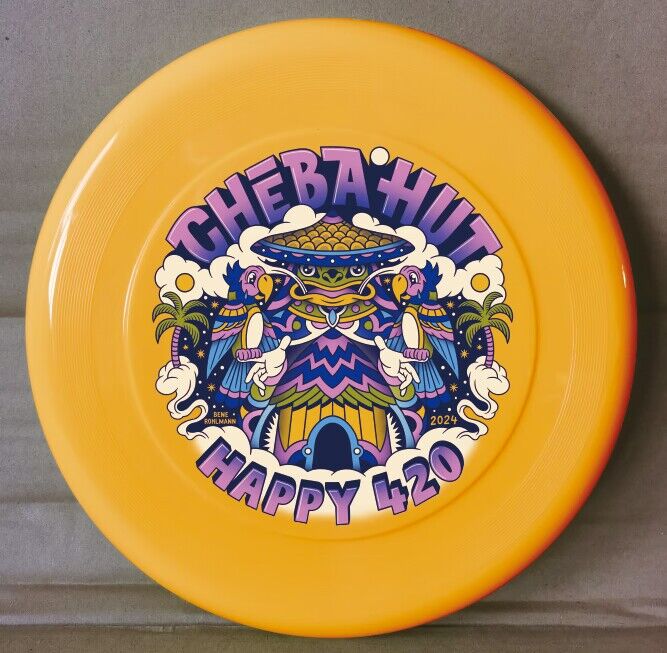 A bright yellow, nine-inch frisbee features a colorful circular graphic in the center. The graphic displays the words "CHEBA HUT" in stylized purple and pink lettering at the top, arching over a central image. This central image is a vibrant, cartoonish depiction of a building with a teal and purple roof, flanked by palm trees, clouds, and what appear to be parrots in shades of pink, blue, and yellow. Below the building, the words "HAPPY 420" are written in large, playful purple letters.