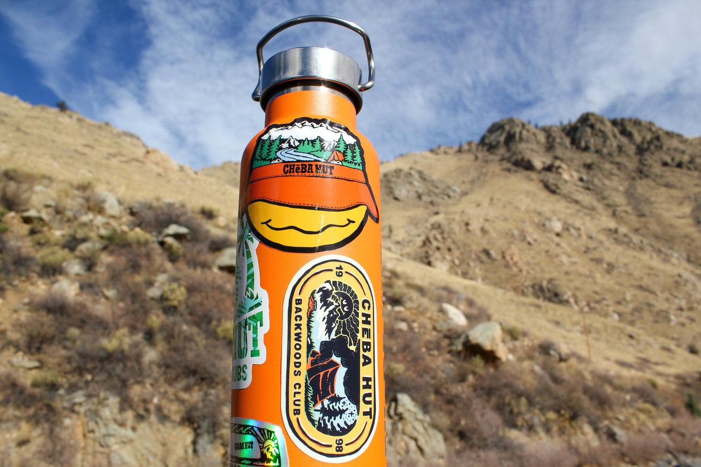 Image of Cheba Hut Backwoods Club Sticker on an orange water bottle with the mountains in the background.